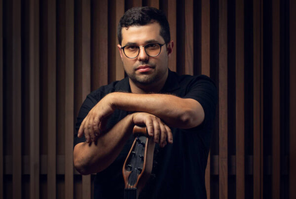 Composer Justin Gray leaning on a bass guitar in front of a brown wood background.