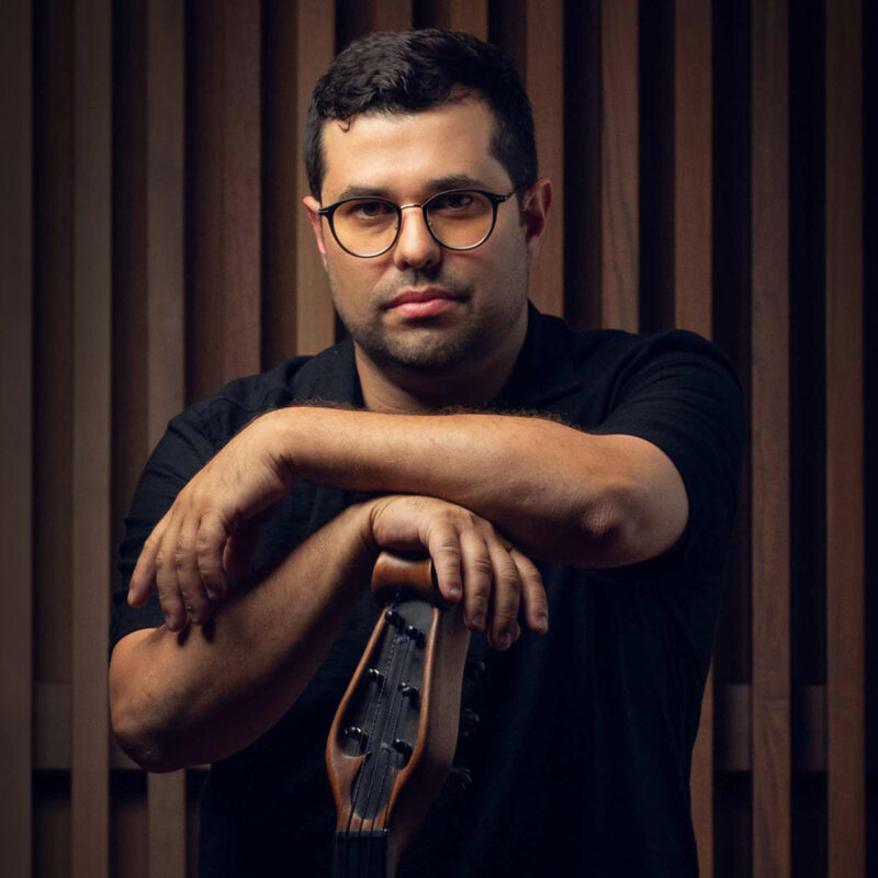 Composer Justin Gray leaning on a bass guitar in front of a brown wood background.